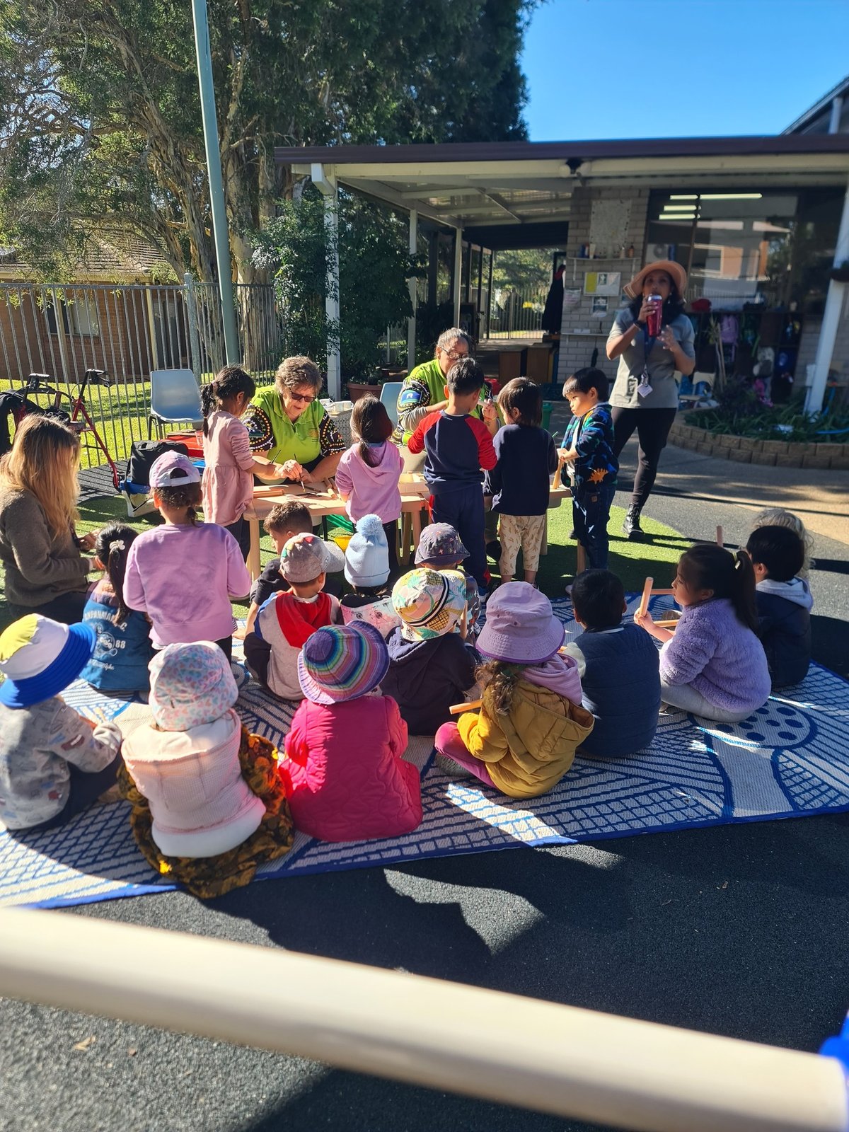 Wolkara Elders sharing culture with young children sitting on a mat outdoors at a preschool.